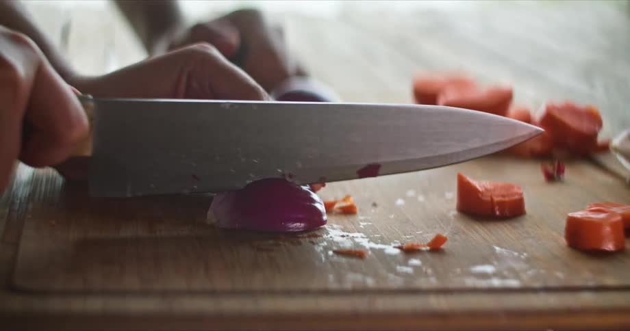 A person cutting onions and carrots on a wood cutting board
