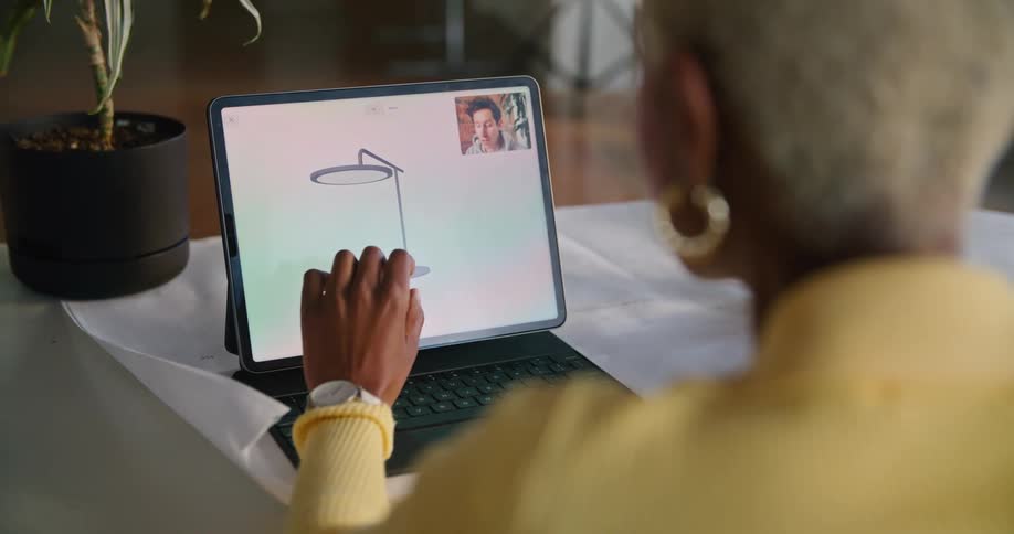 Woman with grey short hair hoop earrings yellow sweater works on laptop making a video call in the office