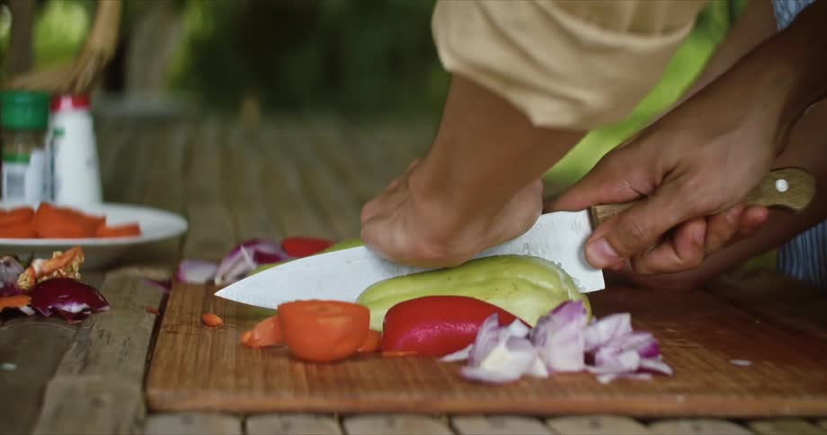 Couple slicing and cutting vegetables with a sharp kitchen knife over a wooden board outdoors