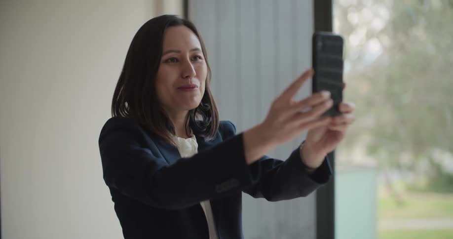 A woman is holding a smart phone in front of it smiling and talking at it