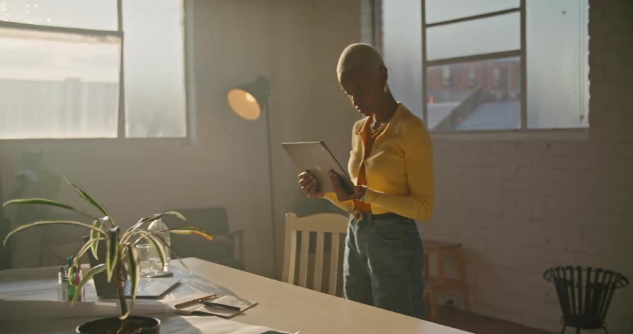 A woman is holding a tablet in front of a desk and filming in a room