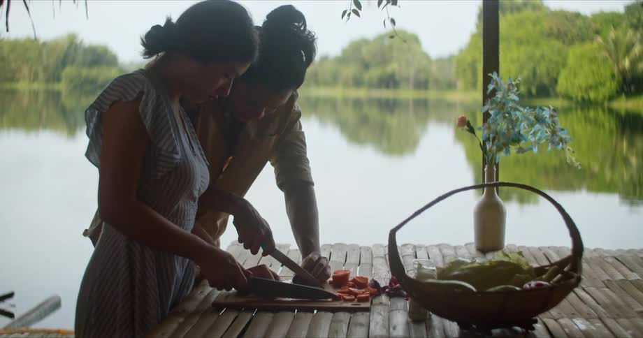Young couple slicing vegetables with kitchen knifes over a board outdoors