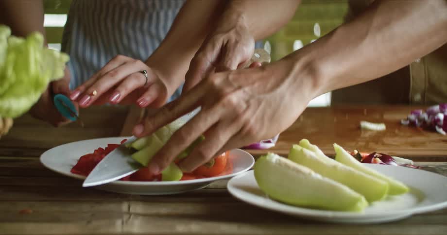 Man with brown shirt and woman with apron put sliced vegetables on plate in the kitchen