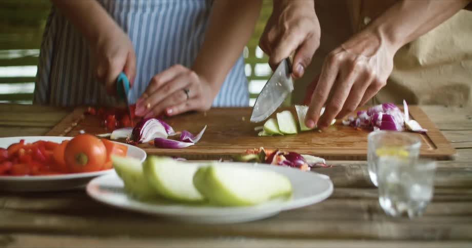 A man and woman are cutting fruit on a cutting board on a table