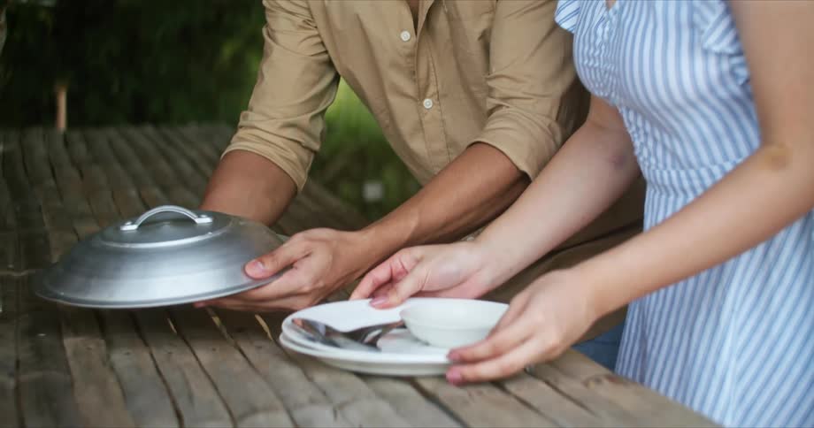 Young couple serving food on a table for lunch in a park outdoors