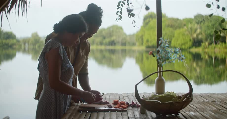 Young couple slicing vegetables over a wooden board near a lake