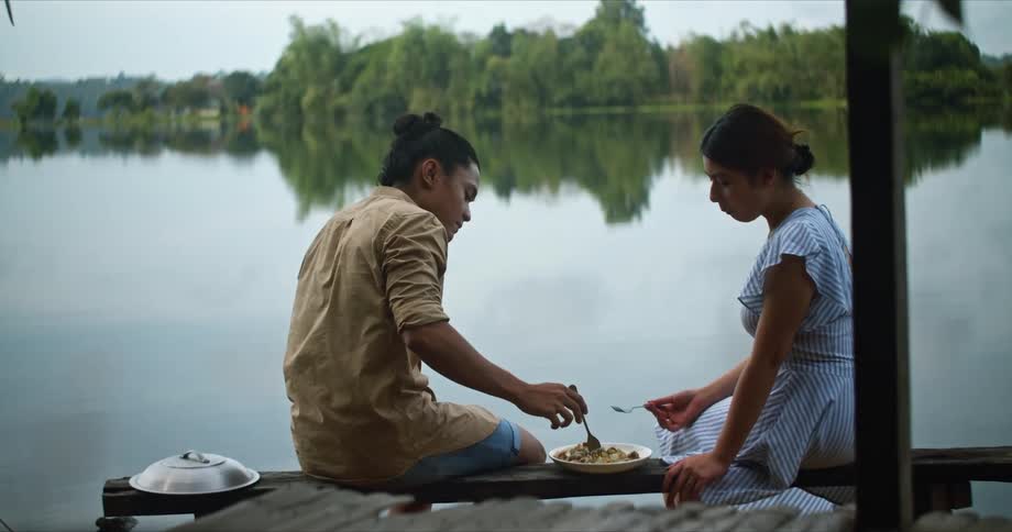 Two women sit together on a wooden landing that overlooks a large lake