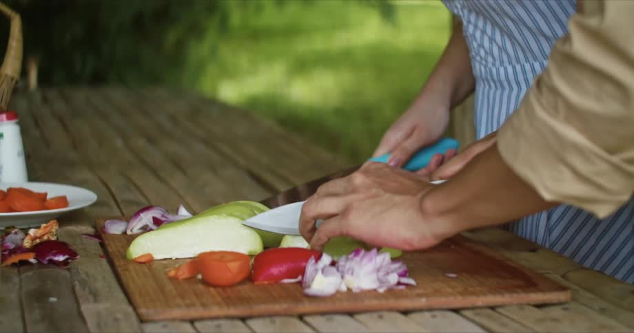 Two people slice and cut fruit and vegetables on a wooden table outside