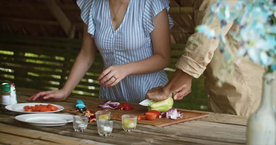 A man and woman stand side by side chopping fresh vegetables on a cutting board