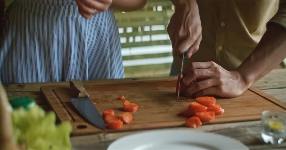 Couple slicing vegetables over a wooden board in the kitchen at home
