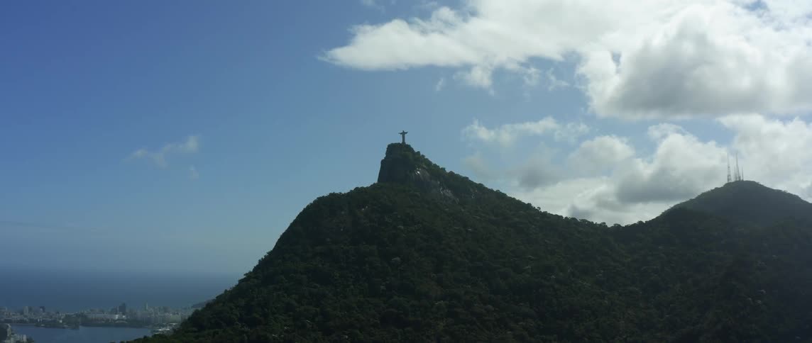A cross is on the peak of a mountain under a cloudy sky