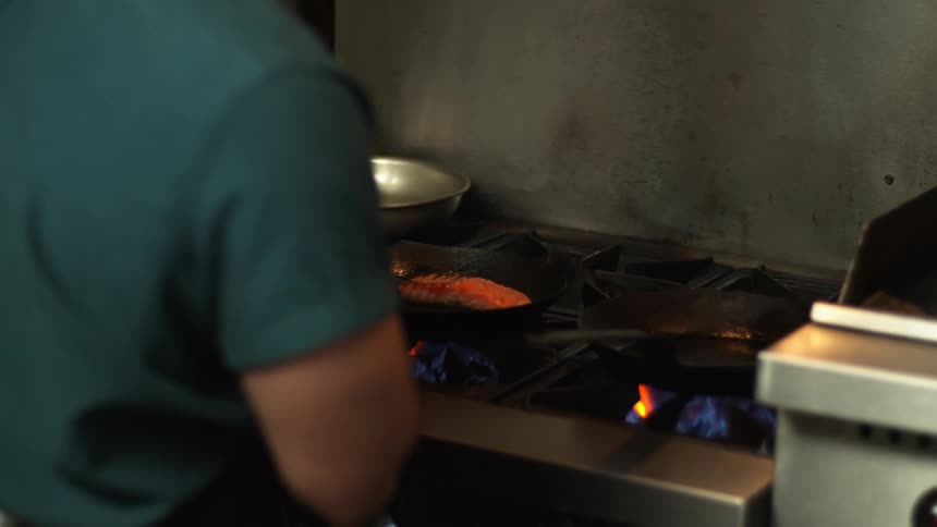 Chef checks meat cooking in skillet on gas burner