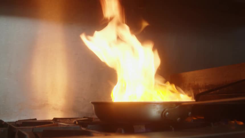 Chef cooks dish in flaming skillet in restaurant stove top