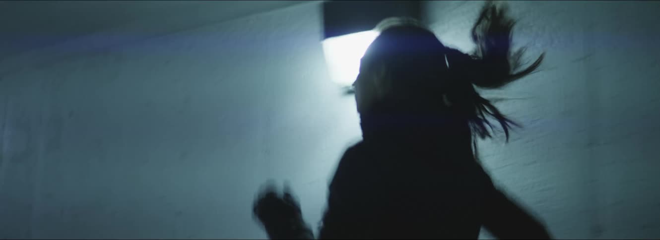 Woman with ponytail and black raincoat runs out of building