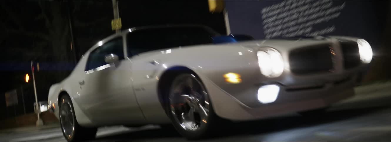 A white muscle car turning onto a city street at night
