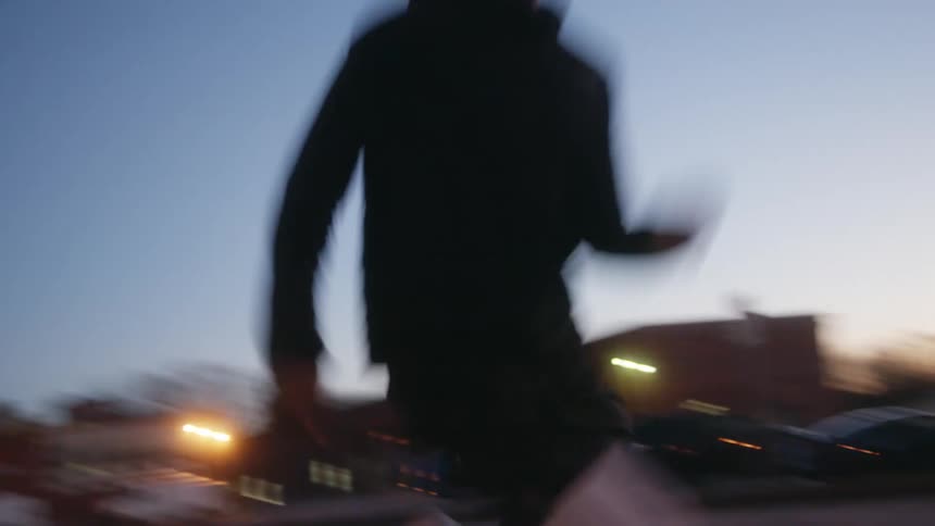Man with black raincoat and shorts jogs in the neighborhood at dusk