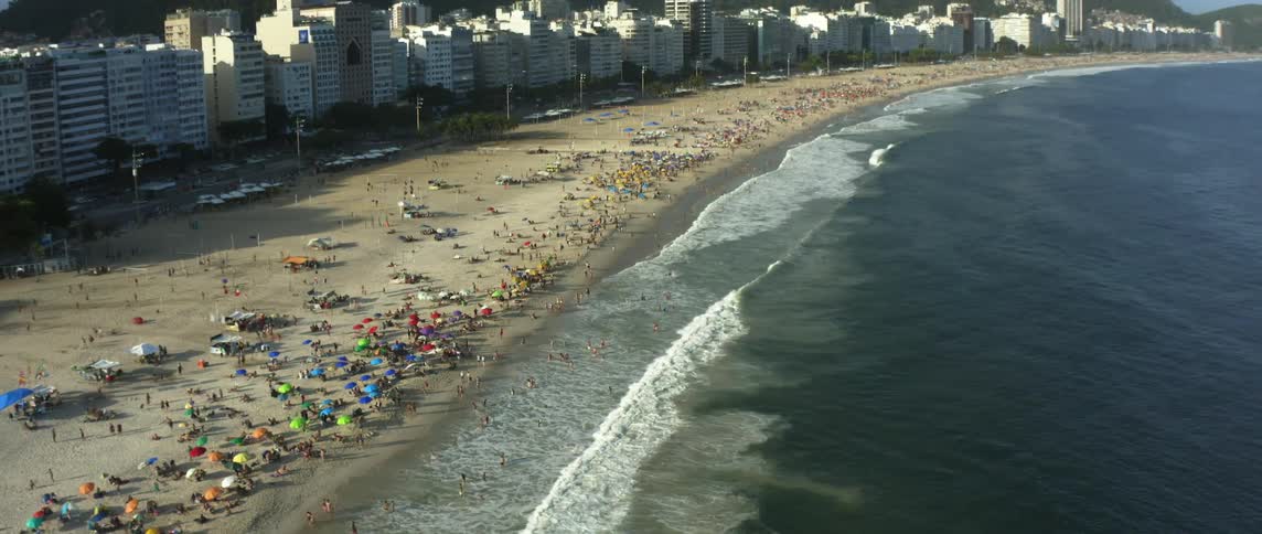 People sunbathing and swimming on a long sandy beach as waves come to shore