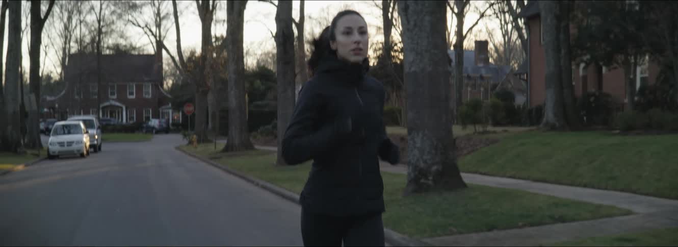 Woman with ponytail and black coat runs down the street at dawn