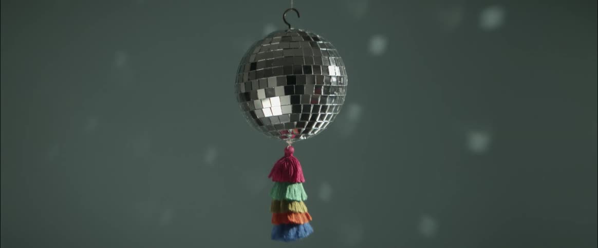 A disco ball with color tassels spins in a room and reflects light against the wall
