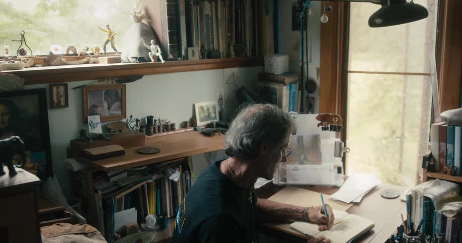A man writes in a notebook while sitting at a desk indoors during the day