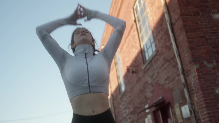 A woman pauses to catch her breath bending over with hands on knees then stretching arms above her head