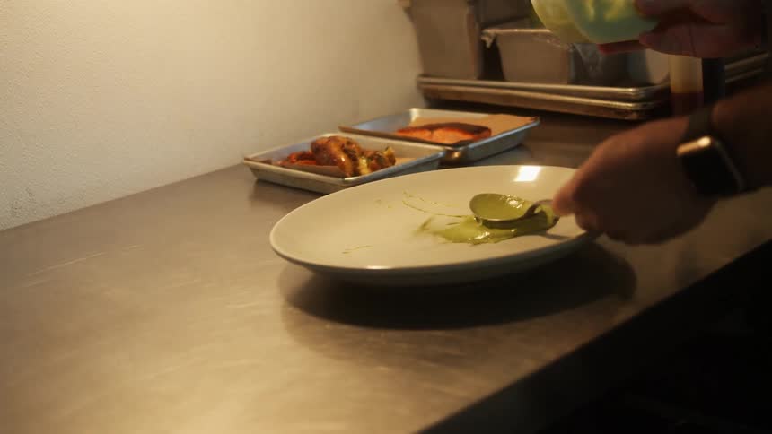 A man pours some sauce on a plate then splashes it for presentation