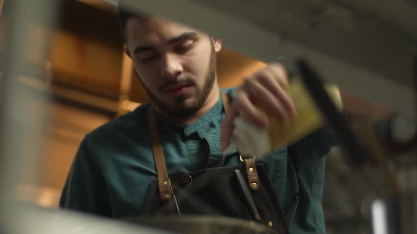 Man with beard and apron adds oil in french fries and takes knife