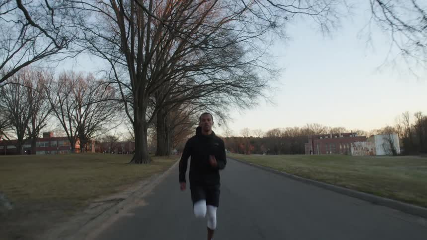 Man runs down road past open fields and under leafless trees away from low office buildings