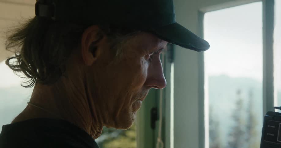 A man holds a small radio up while standing by a window at home