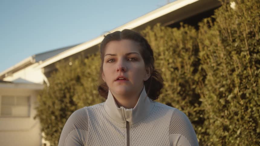 Woman with sport shirt and sport grey shirt crouches down and looks at the camera after working out