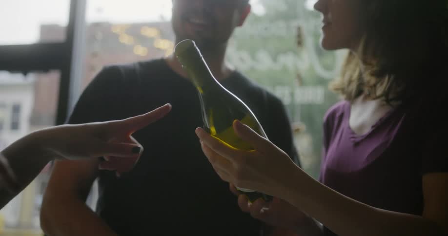 A woman examines a bottle of wine while talking with a pair of friends