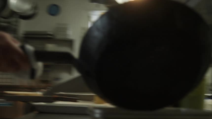 A cook in a restaurant kitchen pours food from a skillet onto a plate