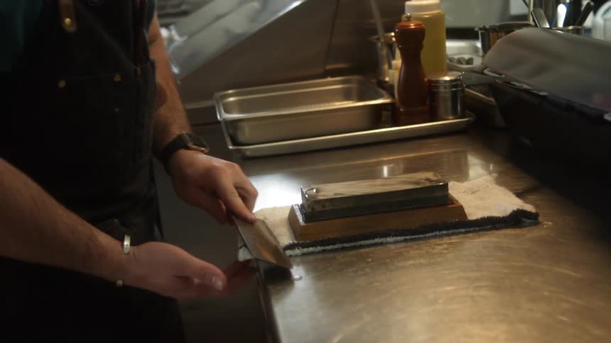 Chef sharpening a cleaver on a wet stone over the counter on a restaurant kitchen