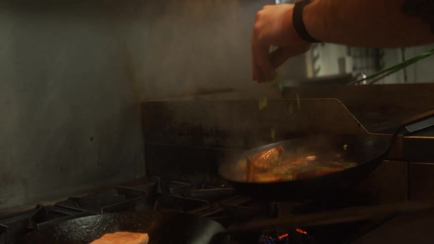 A chef tosses the cooking food in a pan as he adds ingredients