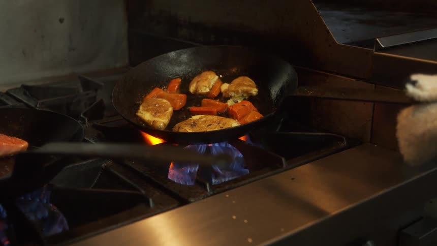 A person is moving a skillet around with food in it over a gas flame