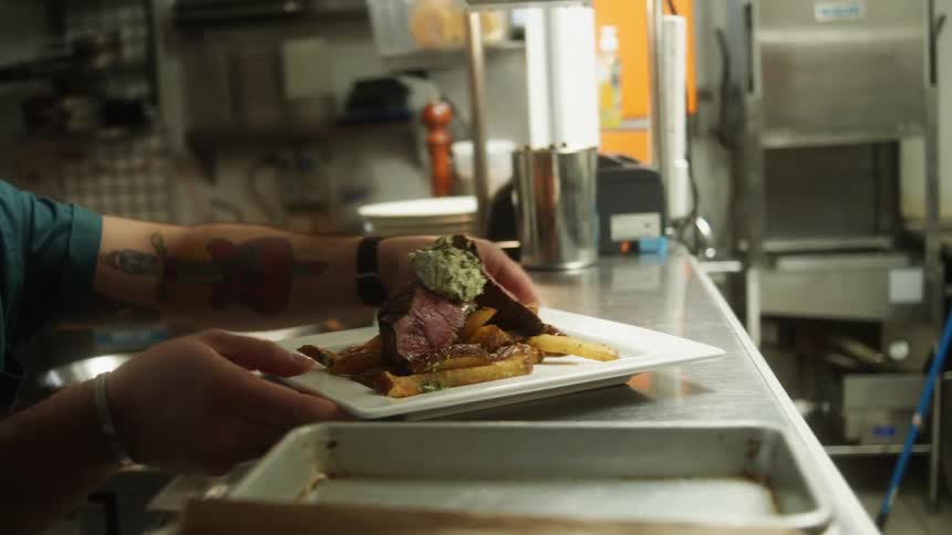 A restaurant cook places a plate of steak and fries on the counter