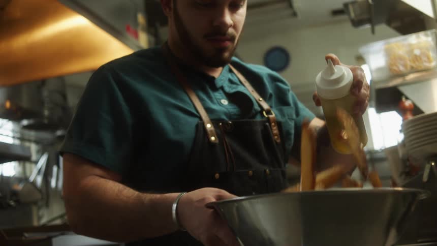 A man in a kitchen adding a liquid to a bowl of crab legs