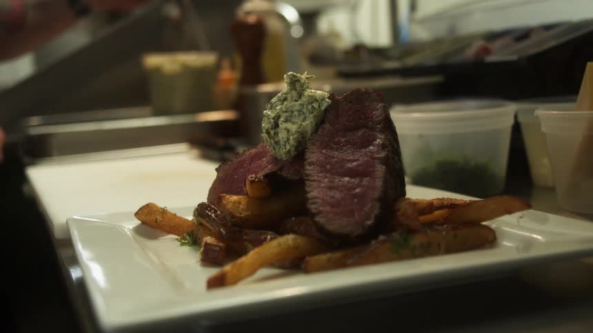 A plated and garnished entre of steak with herb butter on fries