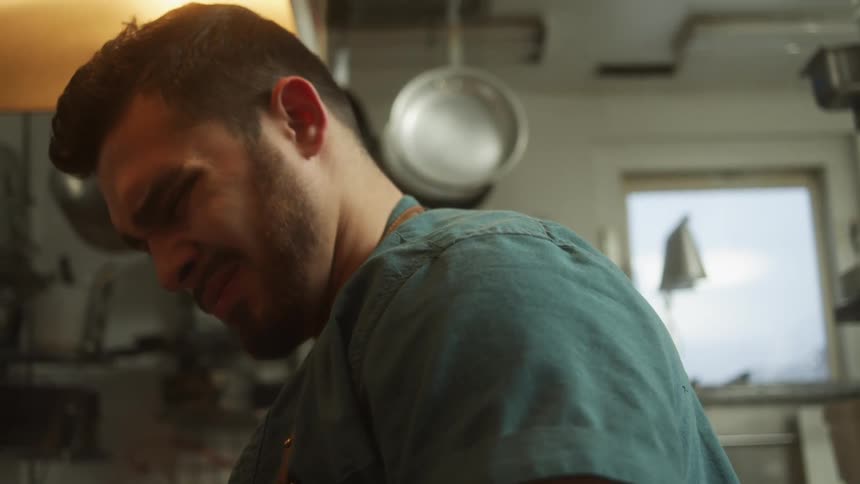 A chef looks down as he stirs and cooks food in a restaurant kitchen