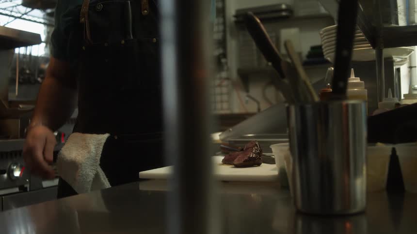Chef serving meat on a white ceramic dish in the restaurant kitchen