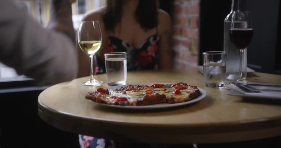 A restaurant server putting pizza on a table in front of a woman