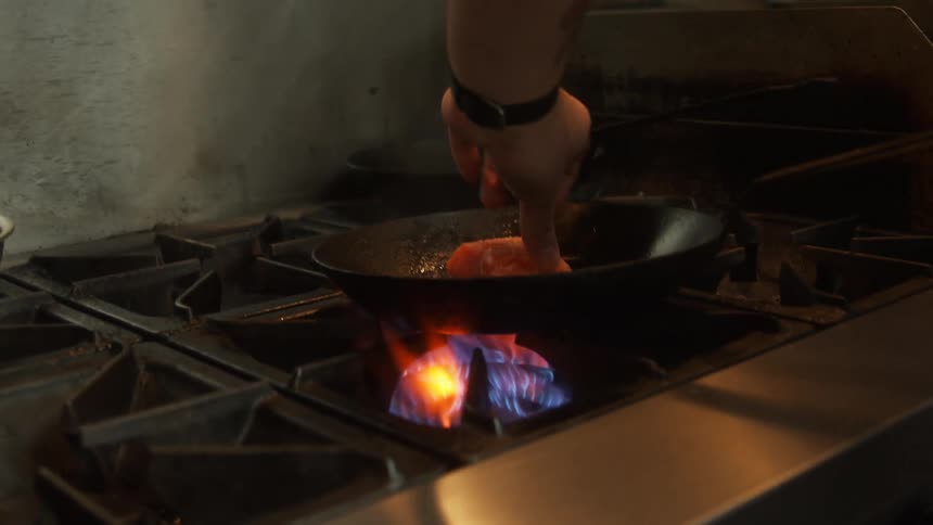 A chef putting fish into a frying pan over a gas burner in a restaurant kitchen