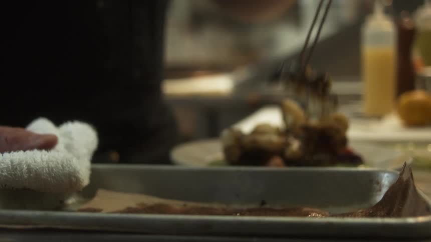 Chef holds roasting pan with towel while dishing out roasted food onto plate