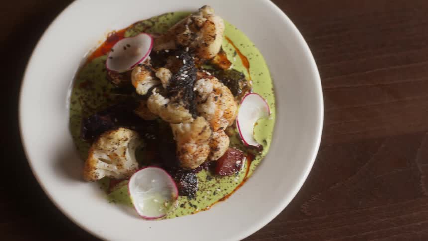 Vegetable dish sits in pale green sauce on white plate on a wooden surface