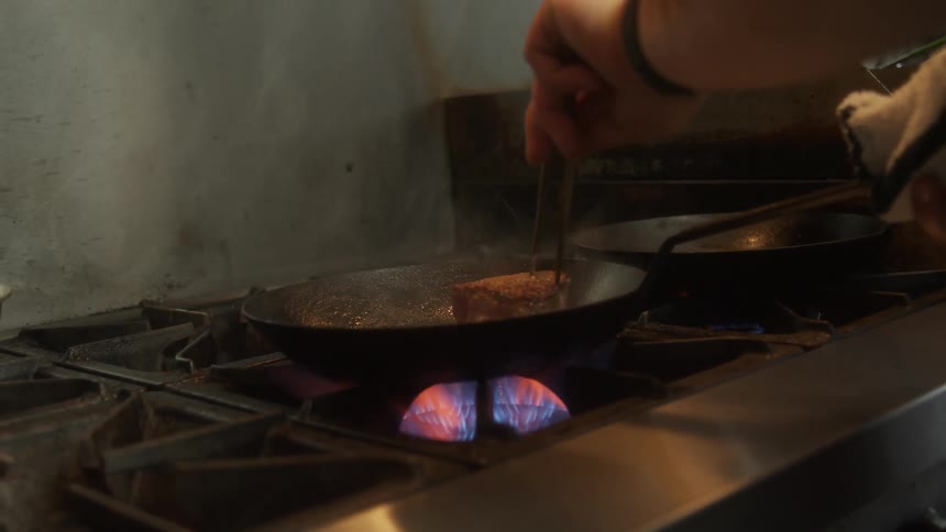 A person is flipping a steak on the pan