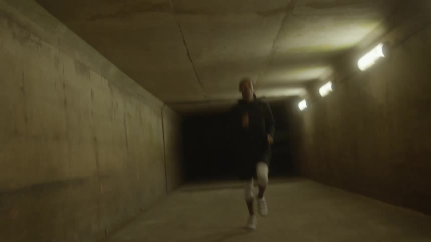 Man with black raincoat and shorts runs through tunnel