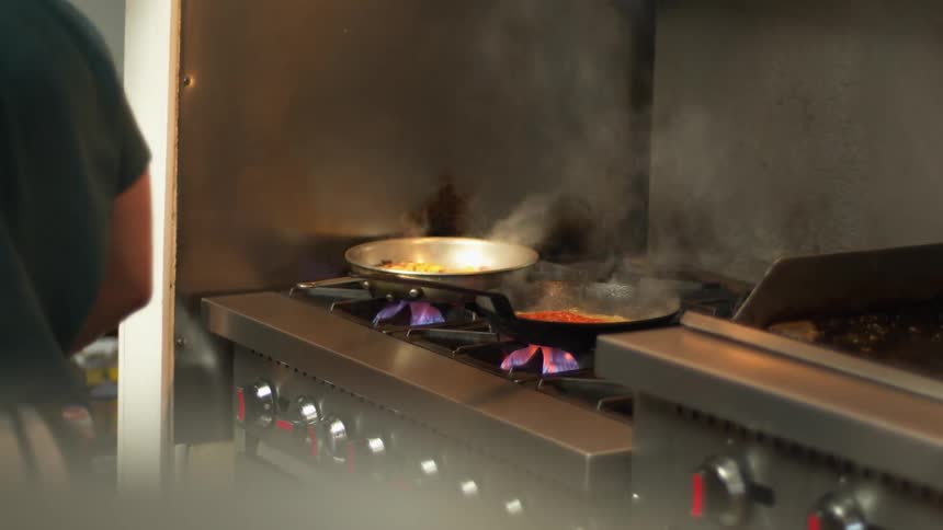 Chef seasoning and flambeing food on a pan over the fire in the kitchen of a restaurant