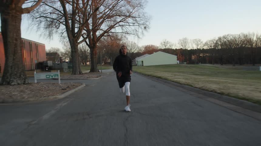 A man runs on an access road past buildings parking lots and grass lawn