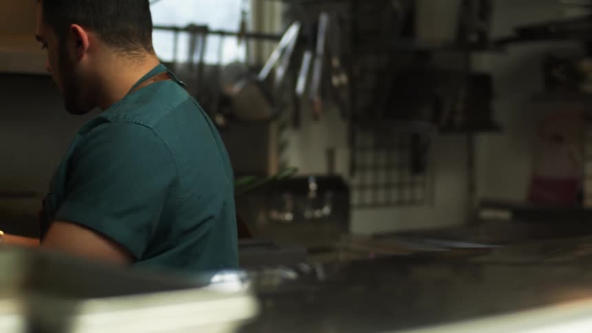 A man uses a grinding mill and turns to a range behind him in a kitchen