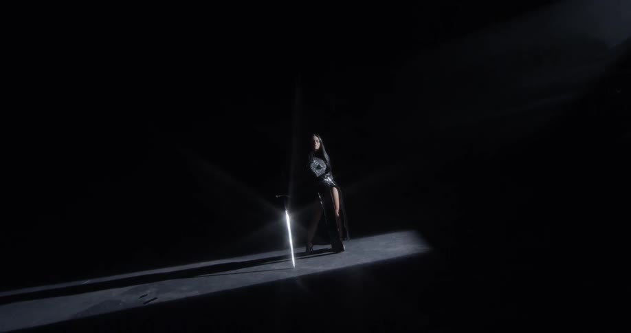 A female stands and poses while holding a large sword that gleams as it reflects the light